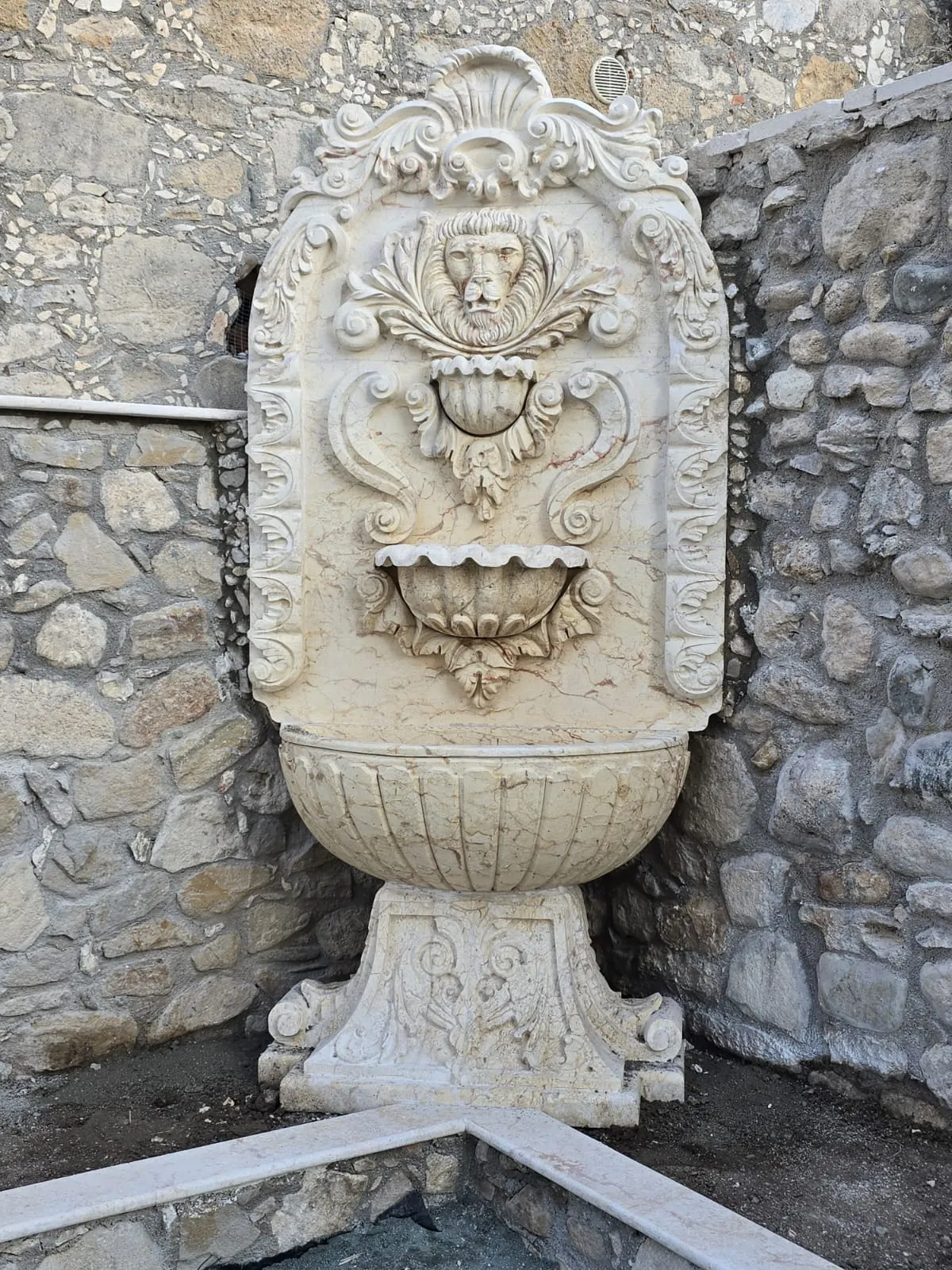 Carved stone wall fountain with a lion mask spout